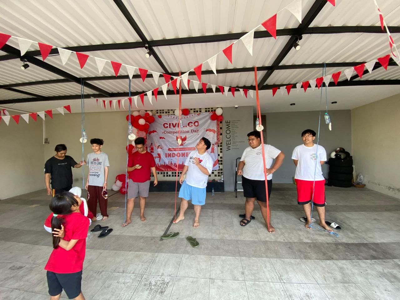 Penghuni mengikuti lomba 17 Agustus di area parkir beratap, dengan bendera segitiga merah putih dan spanduk Civil.co Competition Day