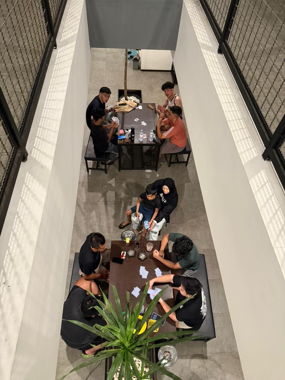 Dilihat dari lantai 2, dua kelompok penghuni bermain kartu di meja courtyard yang diapit railing wiremesh dan dinding beton